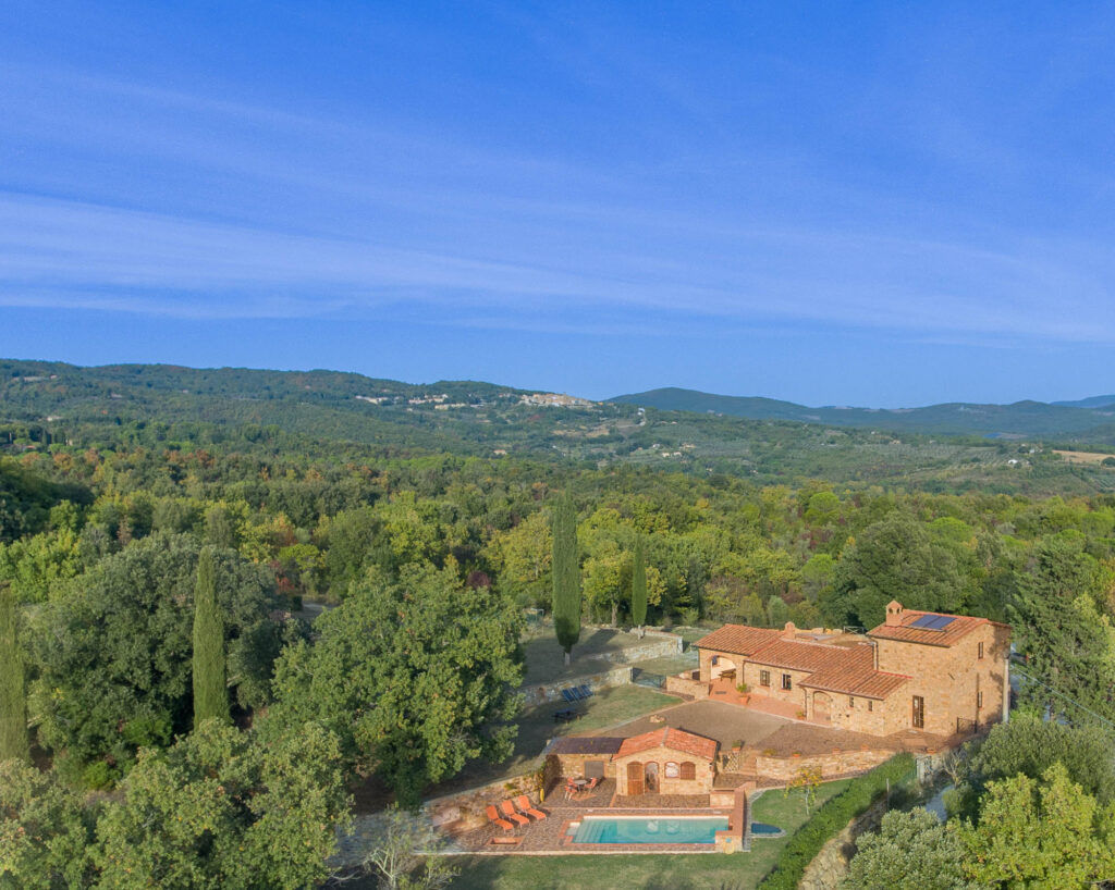 Eine Drohnenaufnahme des Hauses mit Umgebung, Pool und toskanischen Hügeln im Hintergrund.
